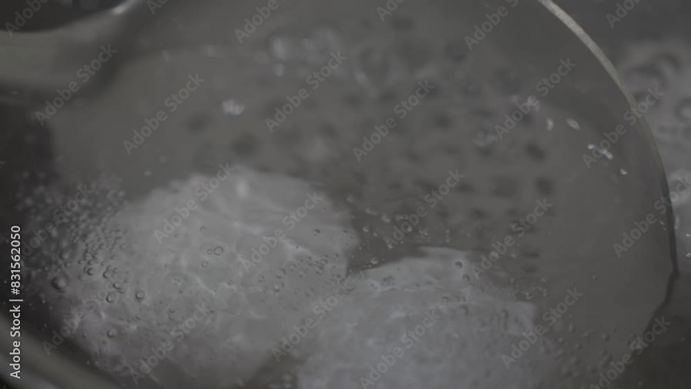 This close up video shows a large industrial kitchen spoon lowering eggs into boiling water. This close up video shows a large industrial kitchen spoon lowering eggs into boiling water.