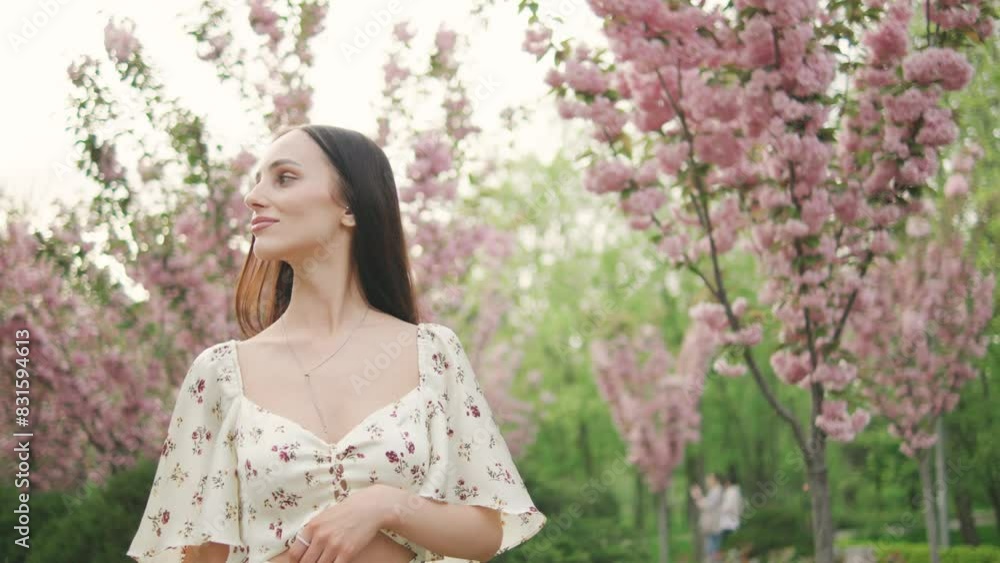 Charming young dark haired woman walking enjoying beautiful sakura flowers in the park Charming young dark haired woman walking enjoying beautiful sakura flowers in the park