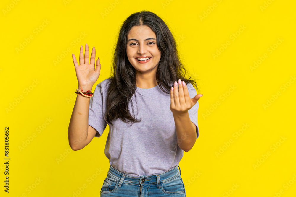 Young Indian woman smiling friendly at camera, waving hands gesturing hello greeting or goodbye welcoming with invitation hospitable expression. Arabian Hindu girl isolated on yellow studio background Young Indian woman smiling friendly at camera, waving hands gesturing hello greeting or goodbye welcoming with invitation hospitable expression. Arabian Hindu girl isolated on yellow studio background