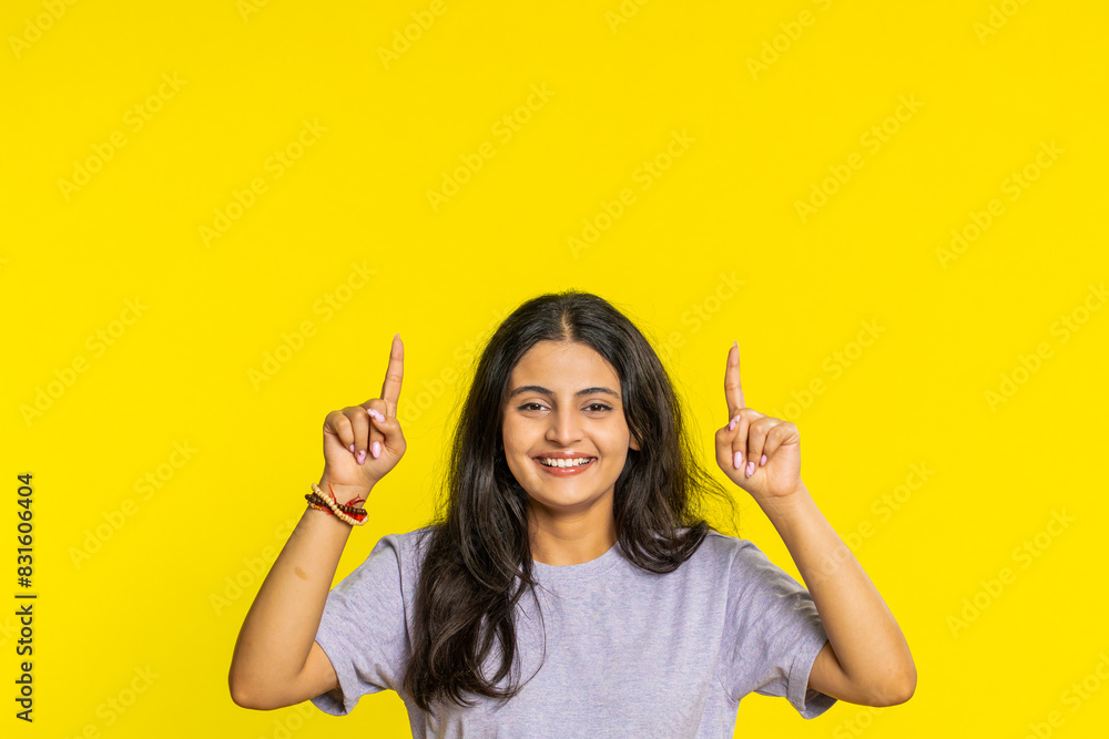 Indian woman showing thumbs up pointing overhead, above head empty place, advertising area for commercial text copy space for goods promotion advertisement. Arabian girl isolated on yellow background Indian woman showing thumbs up pointing overhead, above head empty place, advertising area for commercial text copy space for goods promotion advertisement. Arabian girl isolated on yellow background