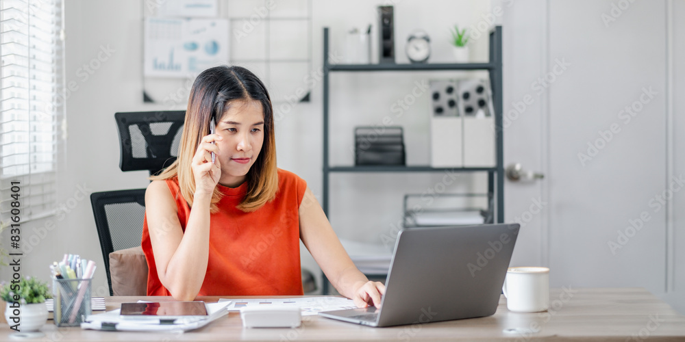 A woman in an orange shirt is sitting at a desk with a laptop and a pen. She is thinking or contemplating something A woman in an orange shirt is sitting at a desk with a laptop and a pen. She is thinking or contemplating something