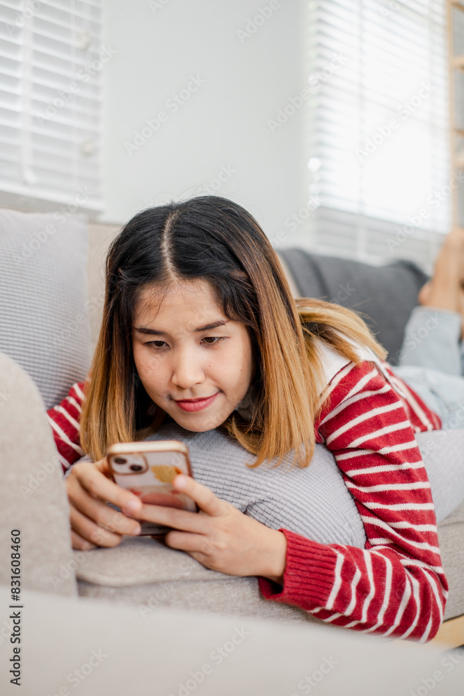 A woman is laying on a couch and looking at her cell phone. She is smiling and she is enjoying herself A woman is laying on a couch and looking at her cell phone. She is smiling and she is enjoying herself