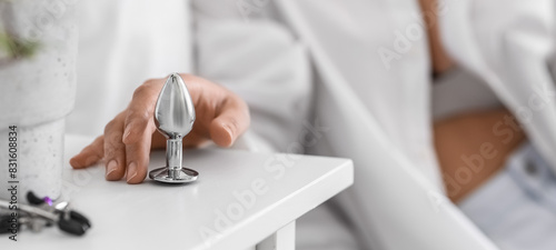 Young woman taking anal plug from table in bedroom, closeup photo