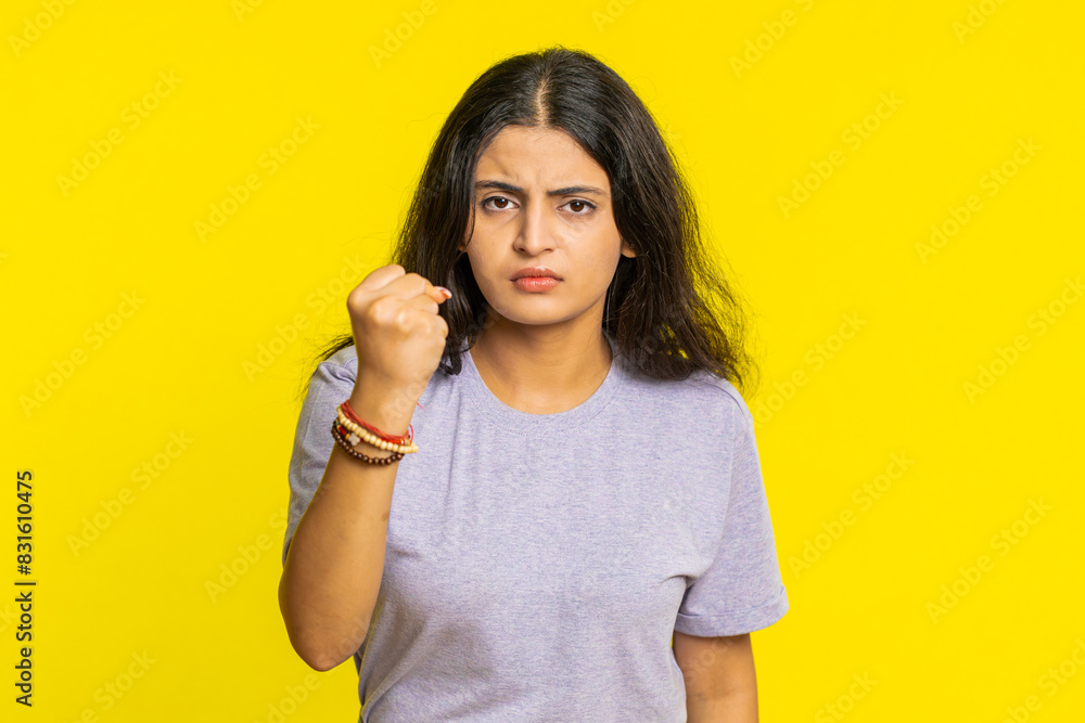 Fototapeta premium Aggressive angry Indian young woman trying to fight at camera, shaking fist, boxing with expression, punishment, threaten, bullying, abuse, mad fury. Arabian girl isolated on yellow studio background
