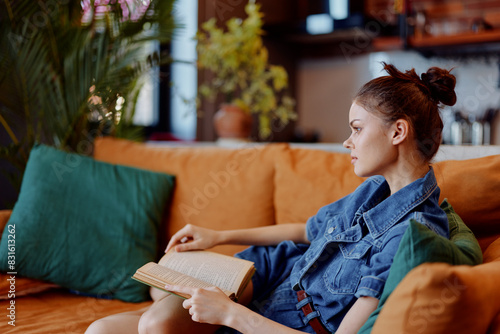 Cuadro en lienzo Woman sitting on orange couch with crossed legs reading book in cozy home interi