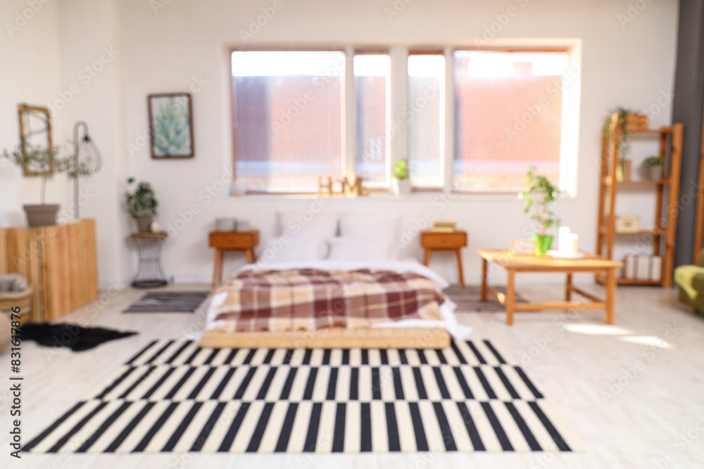 Fototapeta premium Blurred view of light bedroom with bed, tables and window