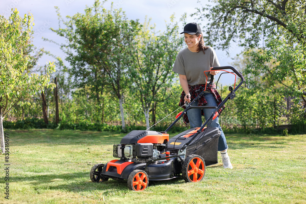 Smiling woman cutting green grass with lawn mower in garden Smiling woman cutting green grass with lawn mower in garden