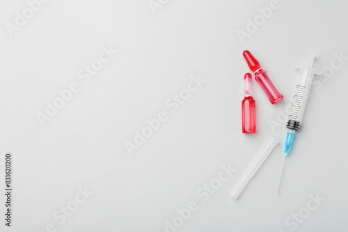Glass ampoules with liquid and syringe on white background  flat lay. Space for text