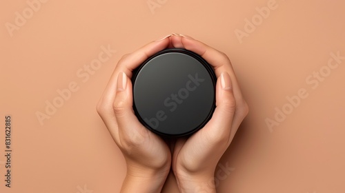 Top and flat view of a woman's hand holding a mockup of a black cosmetic jar on a brown background. Beauty cosmetics product template design, skin care concept