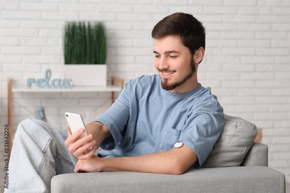 Diabetic young man with glucose sensor using mobile phone for measuring blood sugar level at home Diabetic young man with glucose sensor using mobile phone for measuring blood sugar level at home