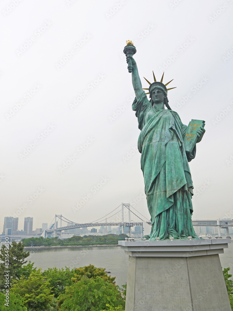 Fototapeta premium Statue of Liberty replica and Tokyo cityscape with famous Rainbow Bridge in background from Odaiba island waterfront