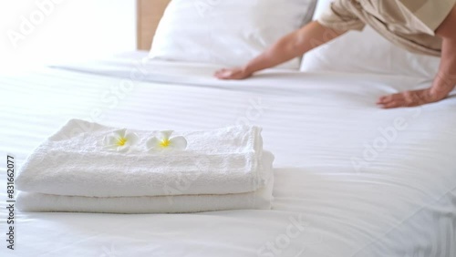 plumeria flower and towels on the bed in the luxury hotel room ready for tourist travel and Hands of the hotel maid clean the bedroom.
