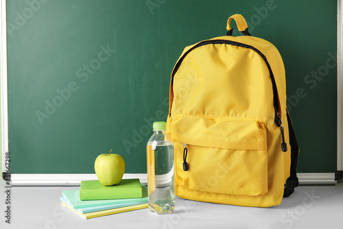 School backpack, notebooks, apple and bottle of water on table against chalkboard