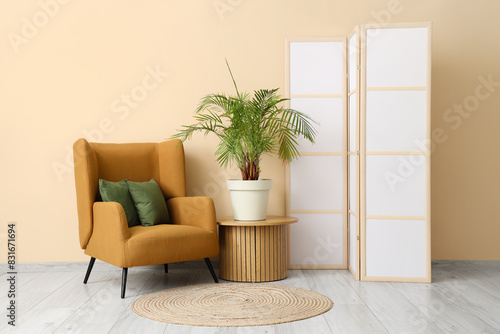 Interior of room with folding screen, armchair and houseplant near beige wall photo