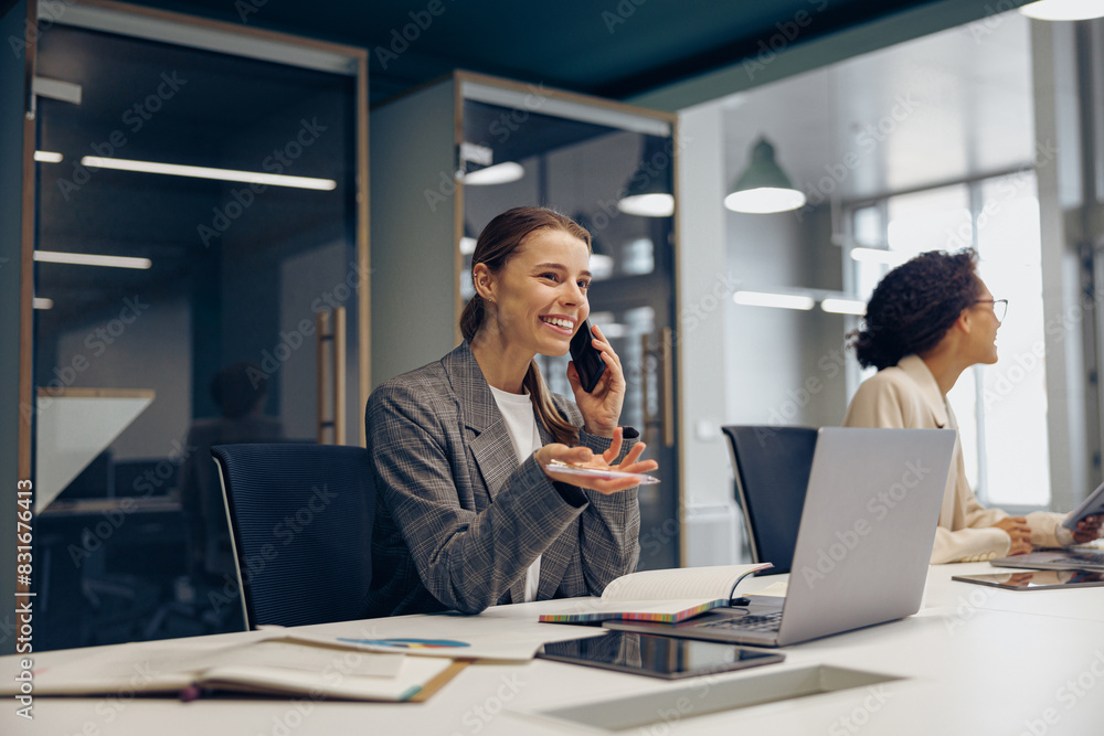 Woman sales manager talking by phone with client sitting in modern coworking and working on laptop Woman sales manager talking by phone with client sitting in modern coworking and working on laptop
