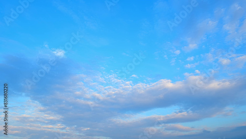 A bright blue sky with a mix of scattered clouds  varying from light and fluffy to more dense formations. The sunlight softly illuminates the clouds  creating a serene and tranquil scene. 