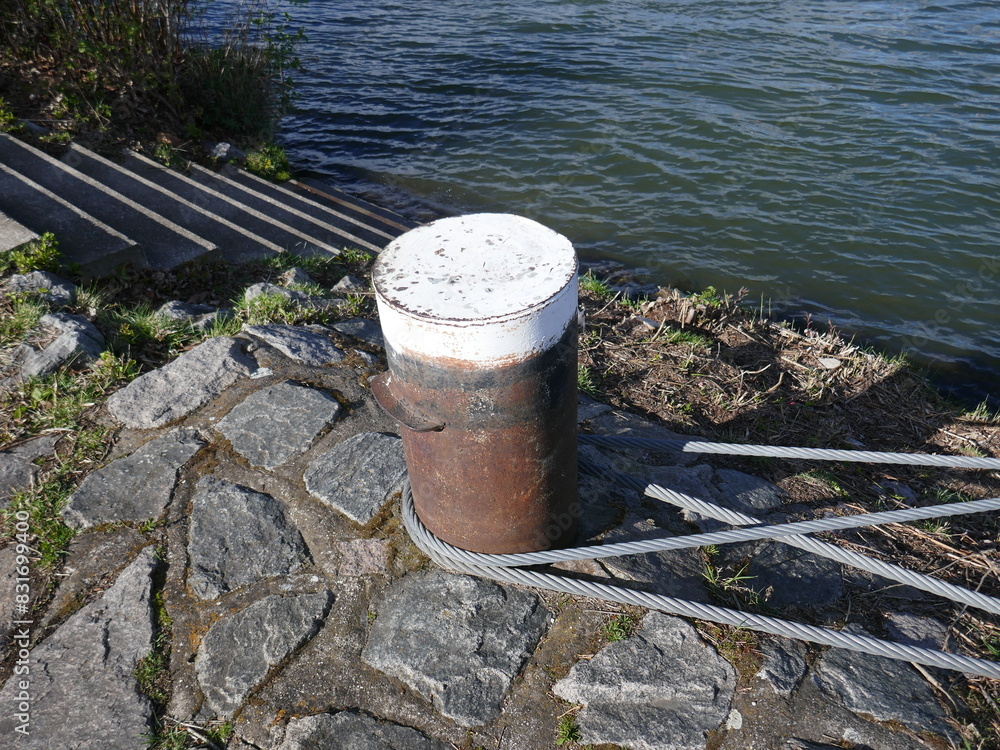 Nautical mooring bollard with lines attached near steps going into water Nautical mooring bollard with lines attached near steps going into water
