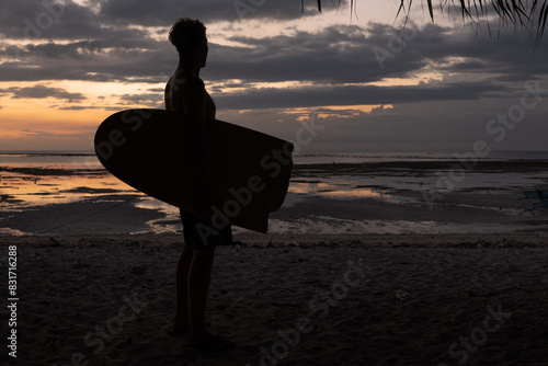 Male surfer with broken surf board under the arm watching the sunset.