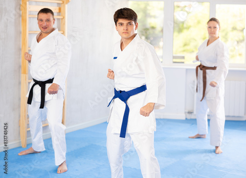 Three athletes have taken starting position and studying and repeating sequence of punches and painful techniques in karate kata technique. Oriental martial arts, training and obtaining black belt