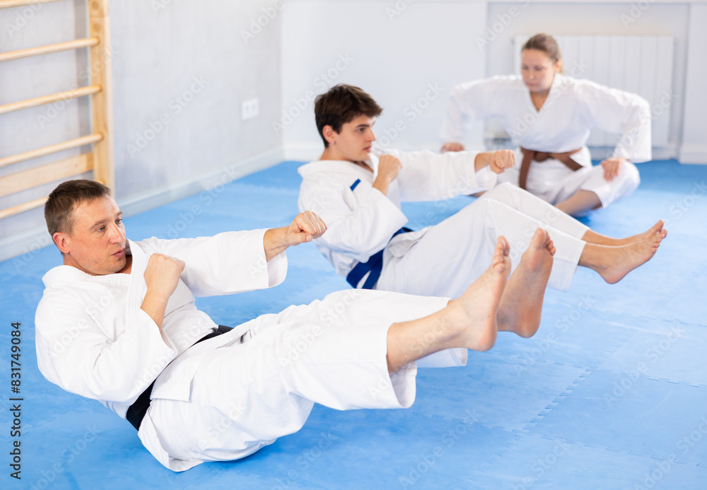 Obraz premium Woman and men in kimono train abdominal muscles and do punches at the same time during karate or judo training