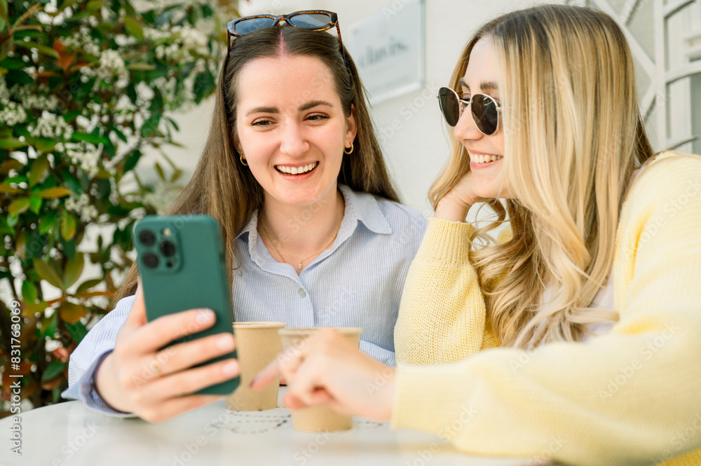 Friends using phone drinking take away coffee in a cafe Friends using phone drinking take away coffee in a cafe
