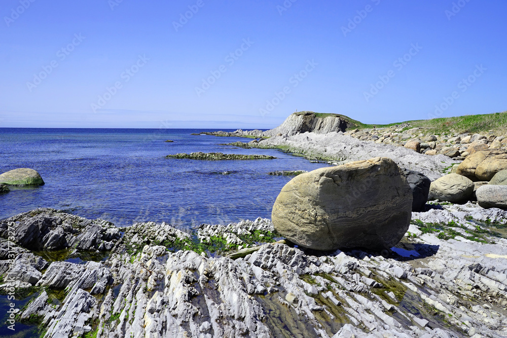 Outcrop by the seaside with a boulder in the foreground and a rocky point in the distance Outcrop by the seaside with a boulder in the foreground and a rocky point in the distance