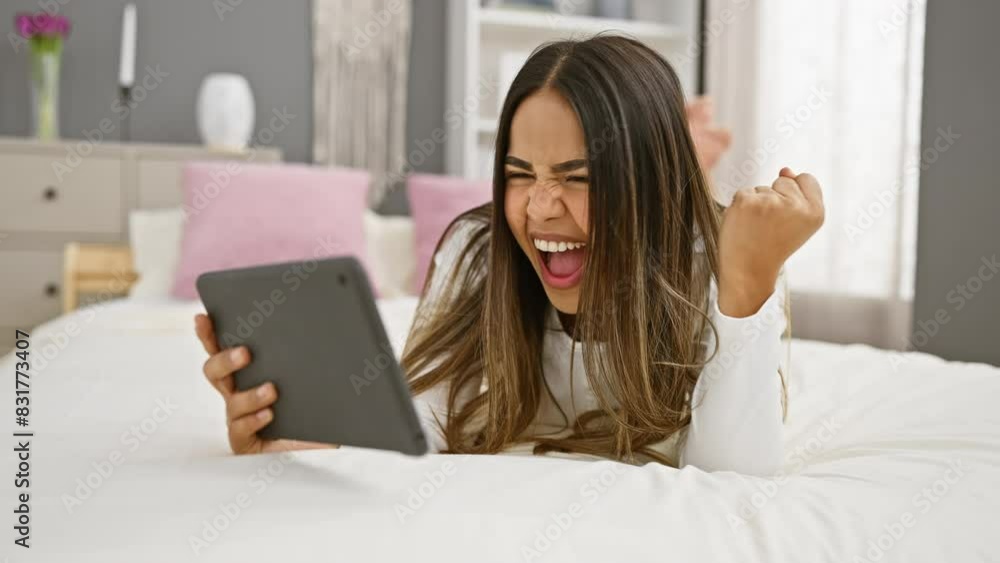 Excited young woman celebrating success with a tablet on a comfortable bed in a well-lit bedroom Excited young woman celebrating success with a tablet on a comfortable bed in a well-lit bedroom