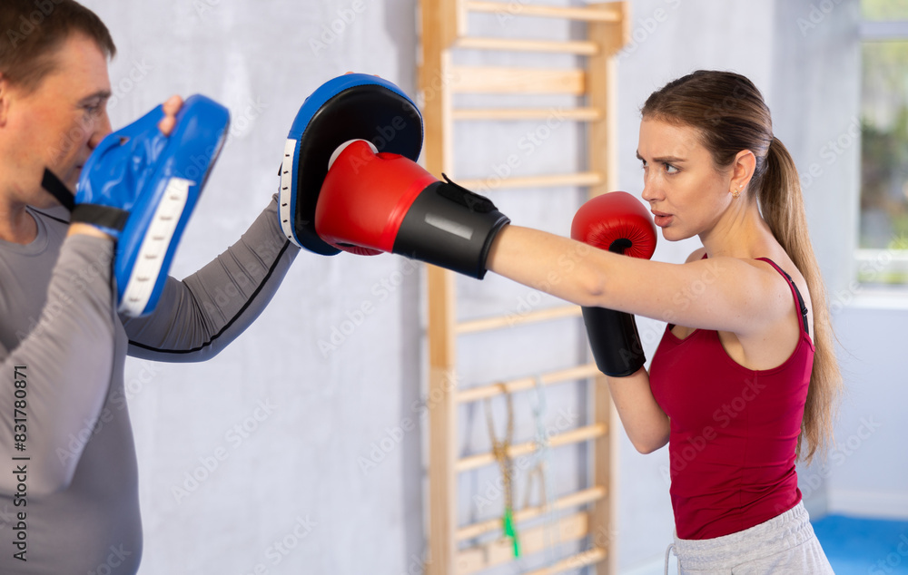 Athletic woman learns to box - hitting punch mitts. Woman with her trainer at the gym