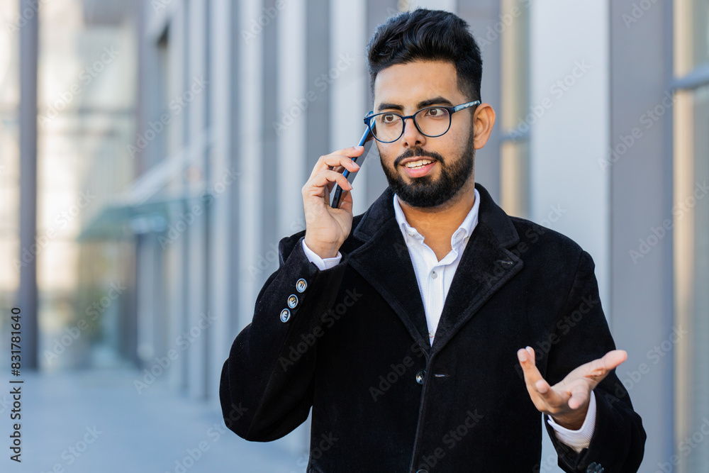 Stylish Indian businessman having remote conversation communicate speaking by smartphone outdoor. Arabian Hindu freelancer guy talking on phone standing downtown city street. Business people lifestyle Stylish Indian businessman having remote conversation communicate speaking by smartphone outdoor. Arabian Hindu freelancer guy talking on phone standing downtown city street. Business people lifestyle