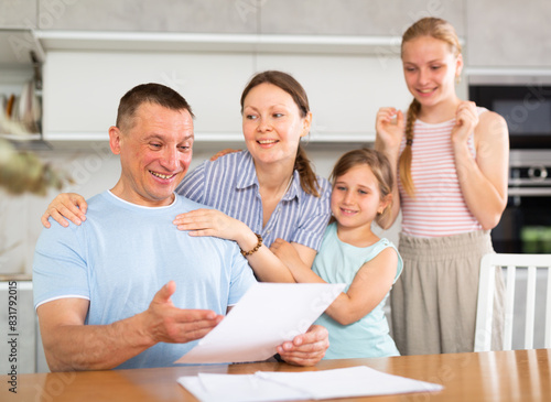Happy family receiving written notification of positive decision from bank or credit organization about approval of loan or mortgage. Cheerful man with wife and teenage daughters reading some papers