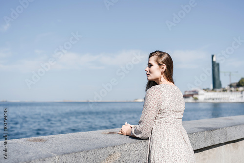 woman stands on a ledge overlooking the ocean. She is wearing a white dress and has her hands on her hips. The scene is peaceful and serene, with the water and sky providing a calming backdrop