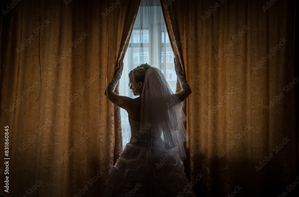 Fototapeta premium Morning of the bride in a white dress and elegant hairstyle. Young attractive, happy girl posing at home. Happiness, purpose and dream wedding.