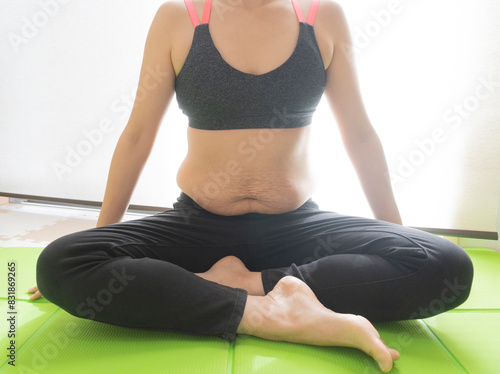 Asian woman in black pants with stretch marks after childbirth practices lotus asana at home. Padmasana pose.