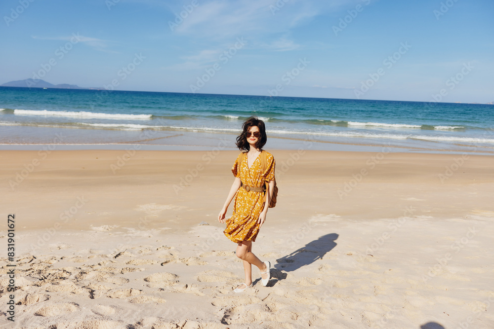 Woman in yellow dress standing on beach looking out at ocean under clear blue sky Woman in yellow dress standing on beach looking out at ocean under clear blue sky