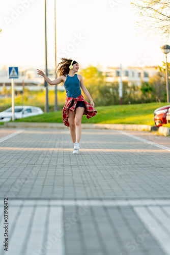 Exuberant young woman with curly hair dances freely on a city sidewalk at sunset, expressing joy. 