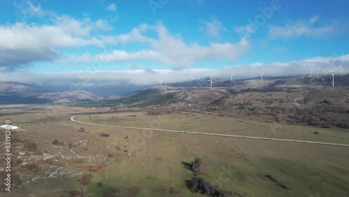 Beautiful aerial shot of Croatian landscape with wind turbines generating renewable energy in the background and an empty road, in the region of Lika in Croatia, Europe (ID: 831912470)