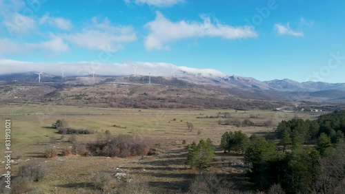 Beautiful aerial shot of Croatian landscape with wind turbines generating renewable energy in the background and an empty road, in the region of Lika in Croatia, Europe (ID: 831913021)
