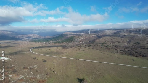 Beautiful aerial shot of Croatian landscape with wind turbines generating renewable energy in the background and an empty road, in the region of Lika in Croatia, Europe (ID: 831914807)