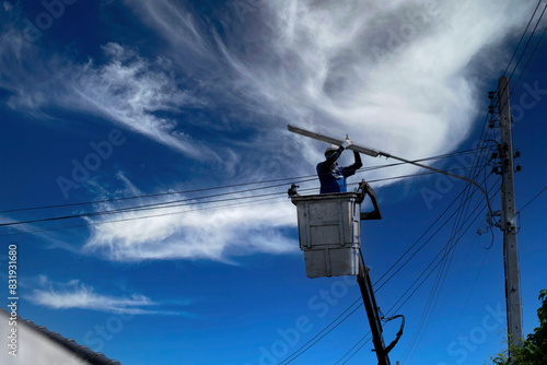 Electrician standing in the basket of a car fixing a lamp at a power pole