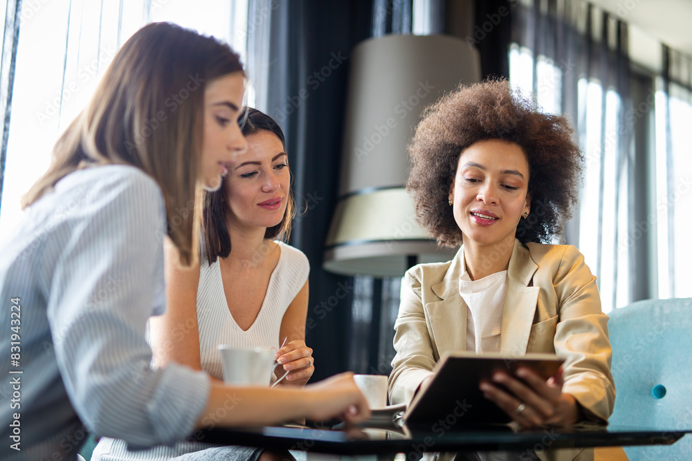 © NDABCREATIVITY - Business woman and her clients discuss business ideas and collaborate over coffee in a cafe.