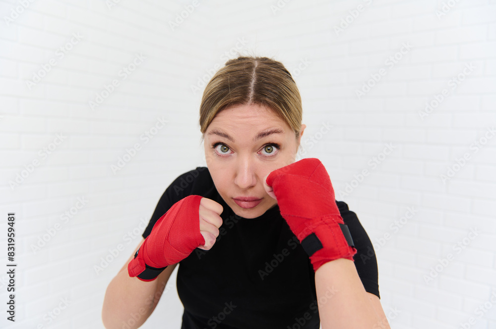 Strong and beautiful European athletic woman, boxer fighter with kickboxing red tapes, doing some boxing exercises, punching forward to camera. Martial art and combat. Wellness, activities and sports. Strong and beautiful European athletic woman, boxer fighter with kickboxing red tapes, doing some boxing exercises, punching forward to camera. Martial art and combat. Wellness, activities and sports.