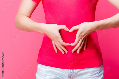 hands of Caucasian Female Girl In Coral T-shirt Posing While Showing Heart Formed Gsture in front of Belly Over Coral Pink
