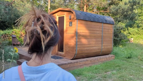 A personal small hotel sauna. Mobile compact bath in the form of a wooden barrel. SPA, relax. Back view of the caucasian woman walking in forest