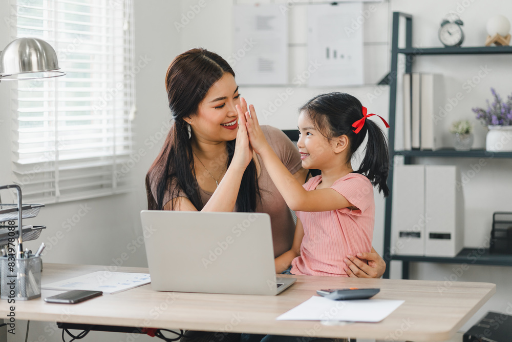 Young mother working on laptop beside her daughter playing on tablet at home office. Young mother working on laptop beside her daughter playing on tablet at home office.