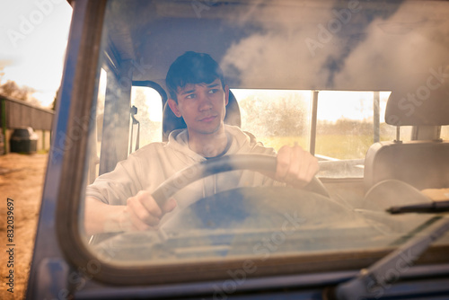 Tableau sur toile Young Male Farm Worker Driving Off Road Farm Vehicle Viewed Through Windshield