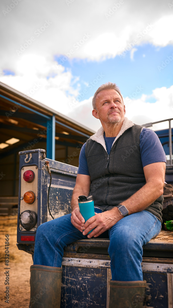 Mature Male Farm Worker Sitting On Tailgate Of Off Road Farm Vehicle Holding Hot Drink In Cup Mature Male Farm Worker Sitting On Tailgate Of Off Road Farm Vehicle Holding Hot Drink In Cup