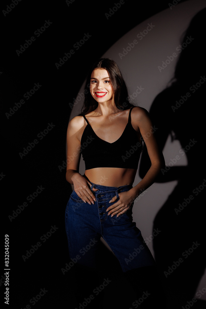 Caucasian woman in a black T-shirt and blue jeans smiling and posing. Portfolio of a model in a photo studio. Caucasian woman in a black T-shirt and blue jeans smiling and posing. Portfolio of a model in a photo studio.