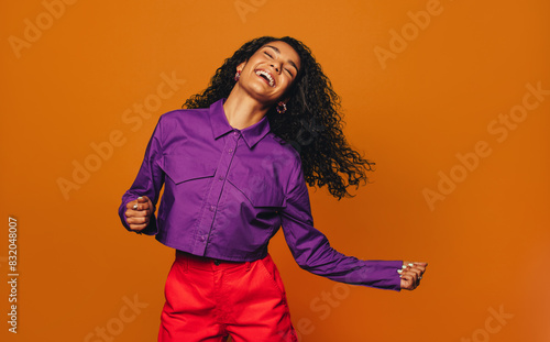Фотография Vibrant woman dancing in casual clothing in a colourful studio with orange backg