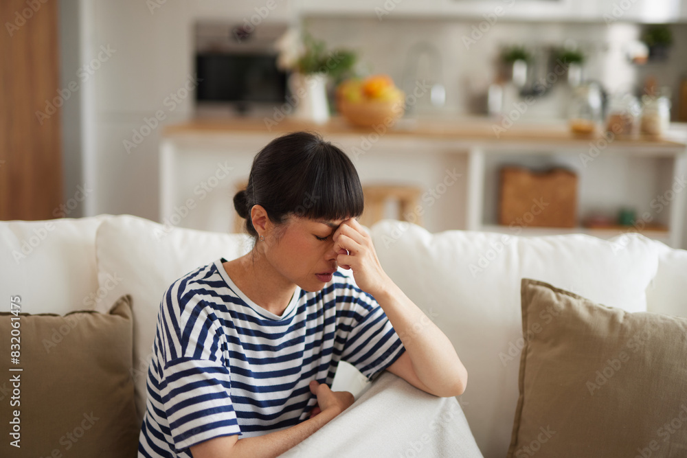 Young Asian woman with headache sitting on couch at home Young Asian woman with headache sitting on couch at home