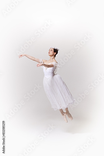 Ballerina in white flowing dress captured in mid-jump, her arms gracefully extended against white studio background. Concept of art, fusion of classic and modernity, grace and elegance.